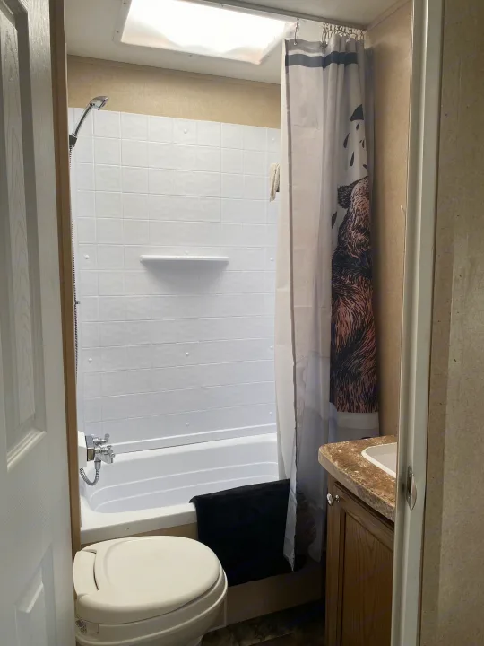 Compact RV rental bathroom with tub/shower, toilet, and sink, featuring a fun bear shower curtain.. Forest River Shasta Revere 2016