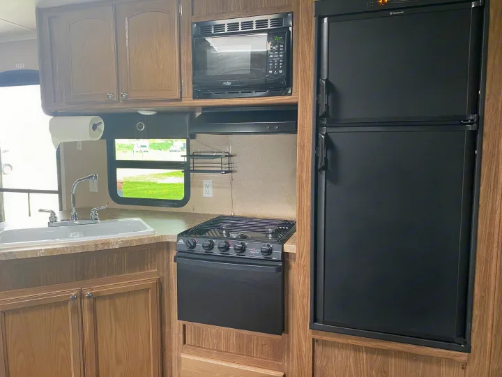 RV rental kitchen: sink, stovetop, microwave, and refrigerator amidst wood cabinets. Ready for your travels!. Forest River Shasta Revere 2016