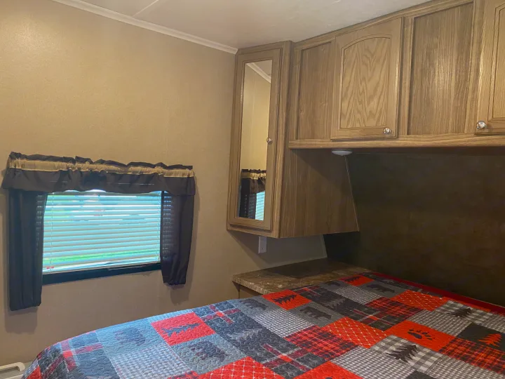 RV rental bedroom: window with blinds, wood cabinets (one mirrored), and a bed with a colorful patchwork quilt.. Forest River Shasta Revere 2016