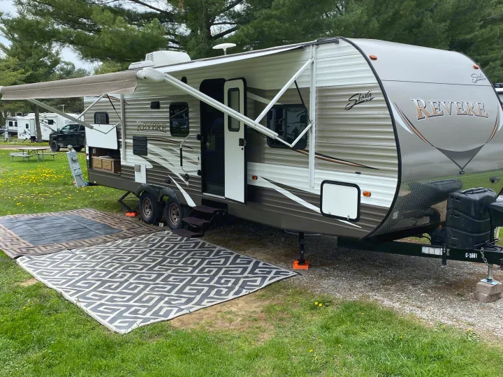 This RV rental, a Shasta Revere travel trailer, is set up with an awning and outdoor rugs at a serene campsite.. Forest River Shasta Revere 2016