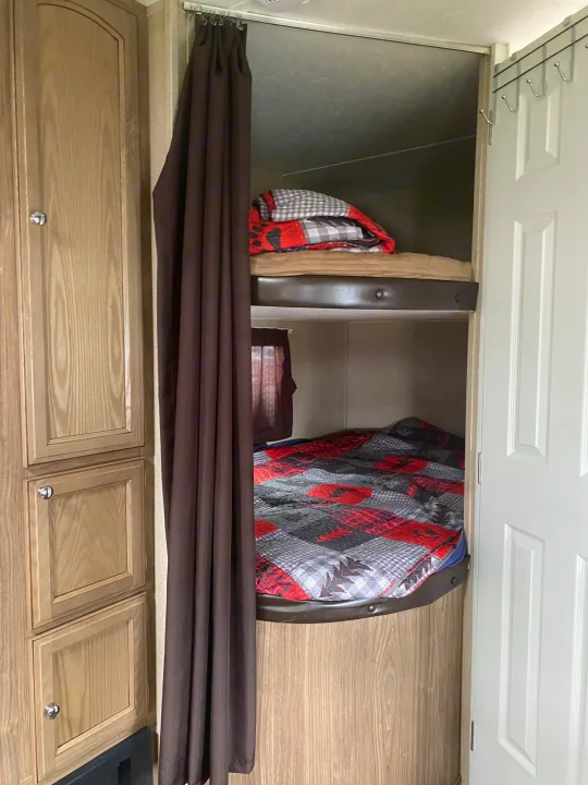 Comfortable RV bunk beds with brown privacy curtain and wood cabinetry. Ideal sleeping space for your next RV rental adventure.. Forest River Shasta Revere 2016