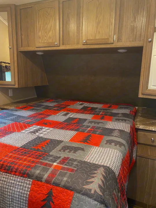 RV rental bedroom interior: a comfy bed with a bear/pine tree quilt, wood cabinets, and integrated lighting for cozy nights.. Forest River Shasta Revere 2016