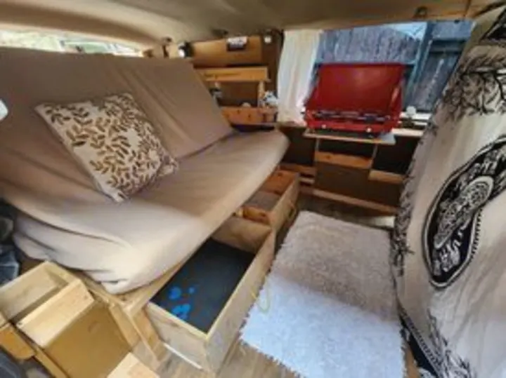 RV rental: Cozy camper van interior with futon bed, pull-out storage, and compact kitchen setup for mobile living.. Chevrolet Open Road 2000