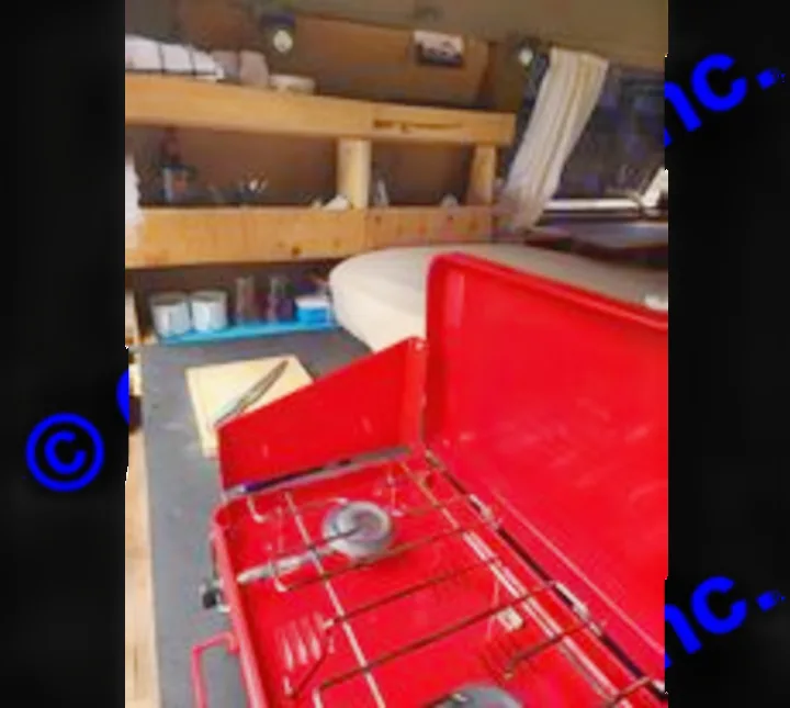 RV rental interior featuring a bright red portable camping stove, cutting board, and built-in wooden shelves.. Chevrolet Open Road 2000