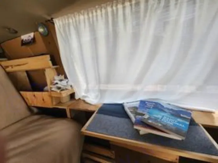 This RV rental's cozy interior features wooden shelving, white curtains, and travel books, perfect for road trips.. Chevrolet Open Road 2000