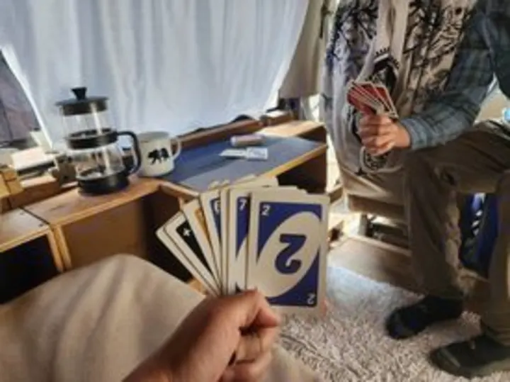 Two people play Uno in a compact RV rental. Card games and coffee make for cozy road trip fun!. Chevrolet Open Road 2000