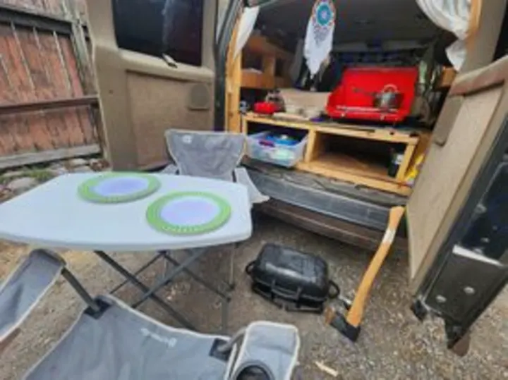RV rental camper van with open rear showing outdoor kitchen setup: portable grill, table, and chairs ready for camping.. Chevrolet Open Road 2000