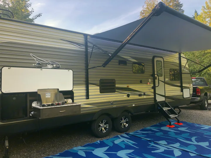 A travel trailer RV rental, equipped with an outdoor kitchen, extended awning, and steps, ready for a camping trip.. Jayco Jay Flight SLX Rocky Mountain Edition 2021