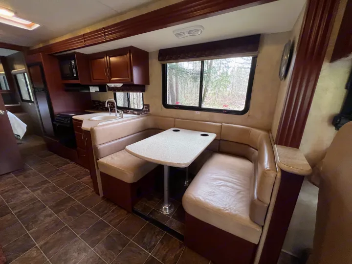 An RV rental's kitchen and dining space, showing dark wood cabinets, a sink, and a light-colored U-shaped dinette.. A.C.E. A.C.E. Motorhome 2013