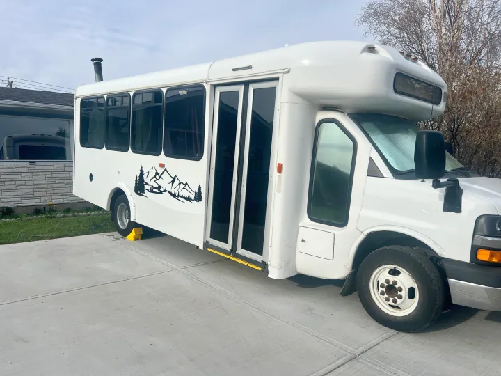 White bus converted RV rental, parked on concrete with a mountain graphic, featuring a roof exhaust.. Chevrolet Express shuttle 2014
