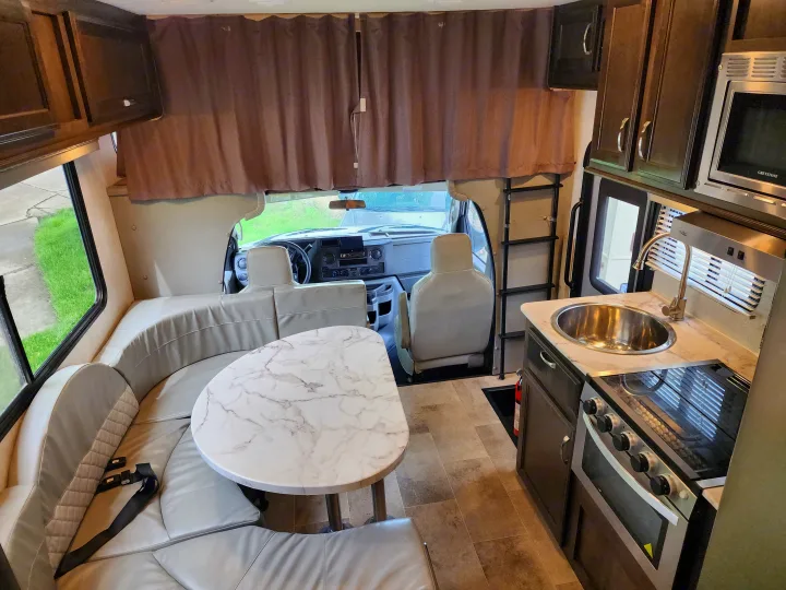 Inside this modern RV rental: a kitchen with sink/stove, dining area with U-shaped seating, and front cockpit.. Gulf Stream Conquest 2021