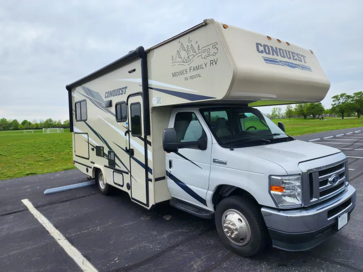 White and beige Conquest motorhome, a Moises Family RV Rental, parked next to a green field under a cloudy sky.. Gulf Stream Conquest 2021