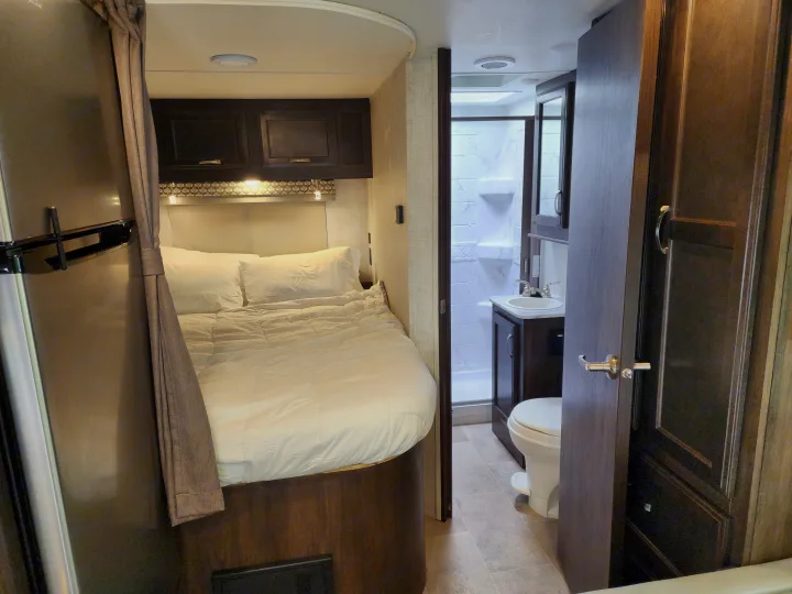 RV rental interior view: a comfortable bed area with cabinets and an adjacent full bathroom featuring a sink, toilet, and shower.. Gulf Stream Conquest 2021