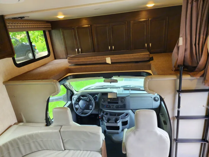 RV rental's front interior with driver's cockpit, dash, and a large cab-over bunk accessible by ladder.. Gulf Stream Conquest 2021