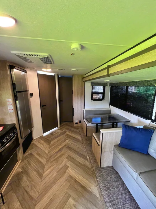 This RV rental interior features a kitchen area with fridge/stove, a dinette, and a sofa lounge. Note the modern herringbone floor.. Heartland RVs Prowler 2022