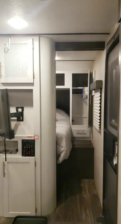 Explore this RV rental's smart interior, with TV, control panel, and a glimpse into the compact bedroom. Perfect for travel.. Keystone RV Bullet Ultra Lite 2020