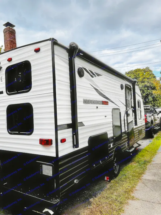 Side view of a large white and black 'Independence Trail' RV rental, hitched to a truck, parked under cloudy skies.. Independence Trail 188DBK 2022