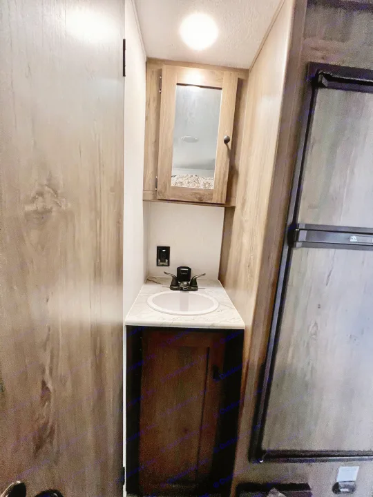 An RV rental bathroom space with a compact sink vanity, medicine cabinet, and built-in refrigerator.. Independence Trail 188DBK 2022
