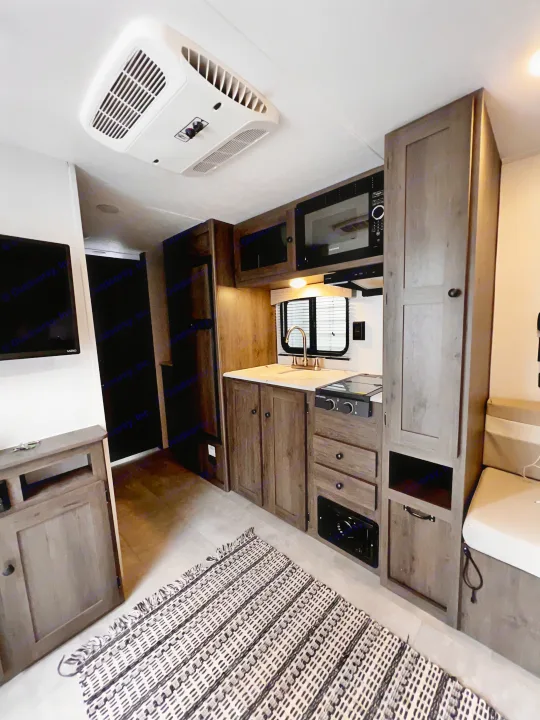 RV rental interior featuring a modern kitchenette with microwave, sink, stove, and a cozy living area with TV and AC unit.. Independence Trail 188DBK 2022