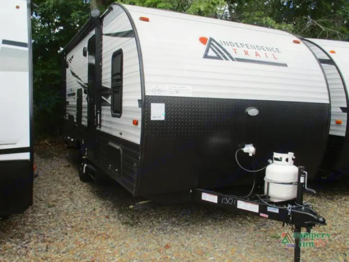A white and black Independence Trail travel trailer RV rental with propane tanks, parked outdoors.. Independence Trail 188DBK 2022