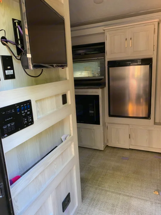 View inside a modern RV rental, showing the kitchen area with Dometic refrigerator, microwave, TV, and central control panel.. Forest River Rockwood Geo Pro 2020