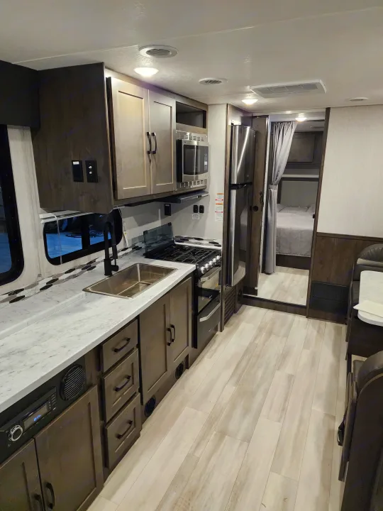 Spacious RV rental interior featuring a full kitchen with microwave & stove, leading to a living area and private bedroom.. Coachmen Leprechaun 2023