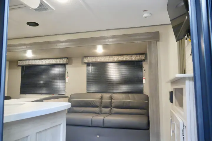 Bright, modern RV rental interior: comfy dark sofa, windows with blinds, ceiling lights, and wall-mounted TV. Ready for your adventures!. Coachmen Other 2023