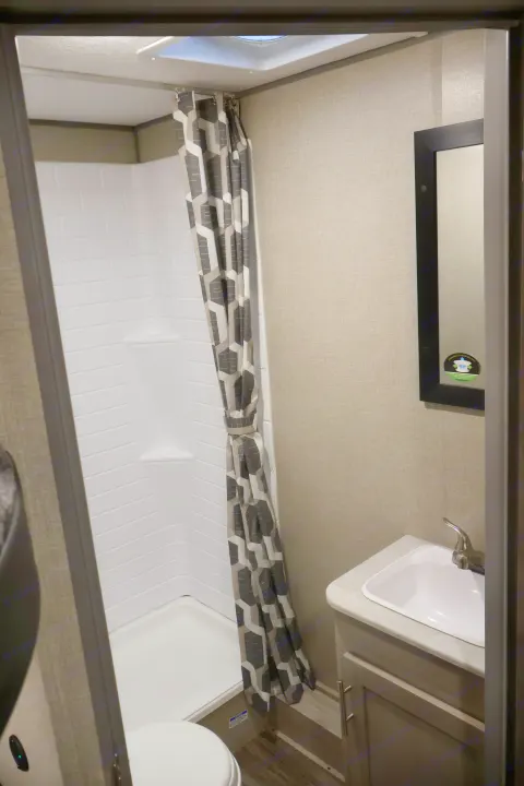 Inside an RV rental bathroom featuring a shower with a geometric curtain, toilet, sink, and mirror.. Coachmen Other 2023