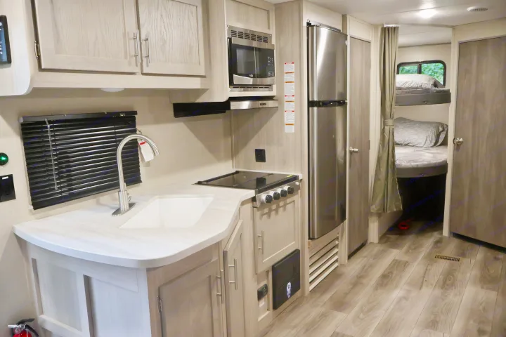 RV rental interior: a modern kitchen with stainless appliances and sink, plus comfortable bunk beds visible beyond.. Coachmen Other 2023