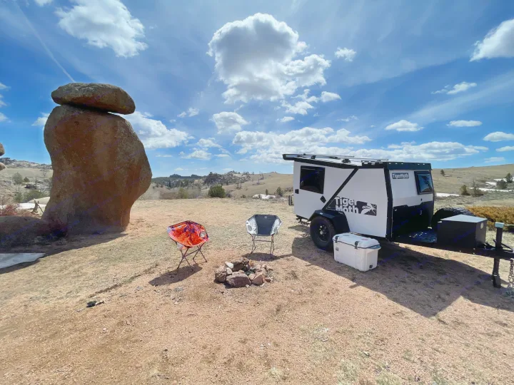 This scenic campsite features an off-road camper trailer, chairs, and fire pit, ideal for an RV rental outdoor adventure.. TAXA Outdoors Tigermoth Camper 2021