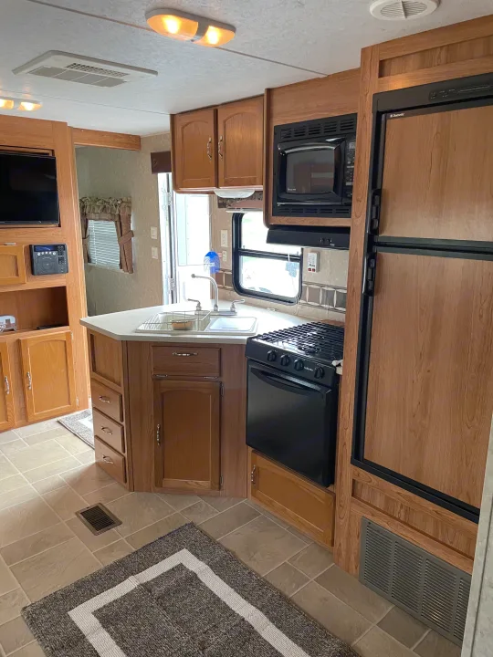 RV rental kitchen: a clean, compact space with wood cabinets, microwave, stove, sink, and fridge. Functional for travel.. Puma 30DBSS 2009