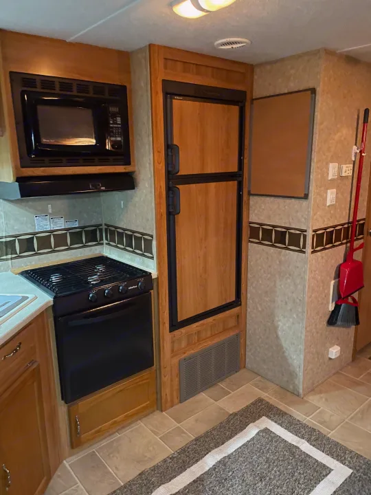 RV rental kitchen view, featuring black microwave, oven/stove, and wood-paneled refrigerator, with tiled floor. Compact and functional.. Puma 30DBSS 2009