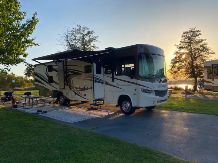 This RV rental is parked at a serene campsite, illuminated by sunset. A Georgetown motorhome, picnic table, and lake are visible.. Forest River Georgetown 2015