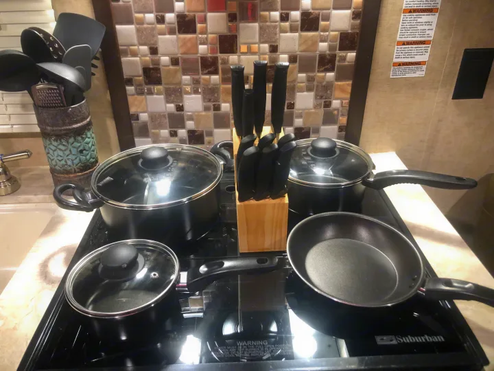 Compact rv rental kitchen with black cookware, knife block, and utensils on a stovetop, set against a mosaic tile backsplash.. Forest River Cherokee Grey Wolf 2018