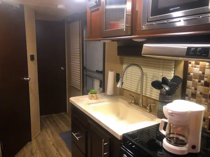 Modern RV rental kitchen with sink, microwave, and coffee maker, showing a hallway beyond.. Forest River Cherokee Grey Wolf 2018