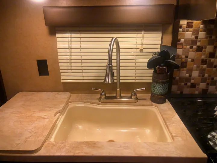 RV rental kitchen: a compact space with a cream sink, modern faucet, light countertop, and window with blinds. Utensils by tiled backsplash.. Forest River Cherokee Grey Wolf 2018