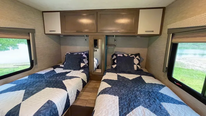 Cozy RV rental bedroom features twin beds, overhead cabinets, and scenic windows.. Thor Motor Coach Four Winds 2021