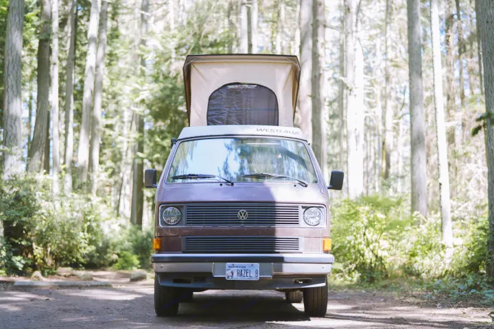 Front view of a Westfalia camper van, perfect for rv rental, parked in a sunny forest with its pop-top extended.. Volkswagen Westfalia 1985