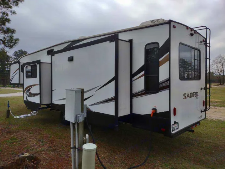 Spacious fifth-wheel RV rental set up at a campsite with hookups. Slide-outs extended for extra room.. Forest River Sabre 2021