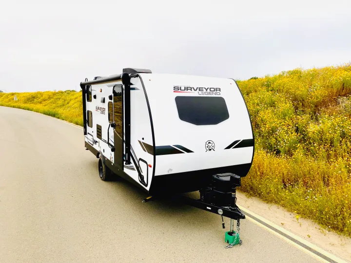 White Surveyor Legend travel trailer, an ideal RV rental, parked on a road lined with vibrant yellow wildflowers.. Forest River Surveyor Legend 2023