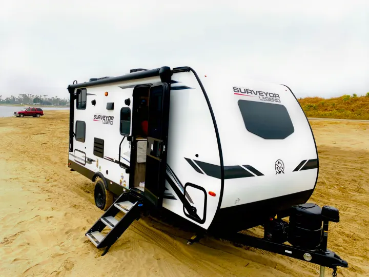 Explore with this white Surveyor Legend travel trailer, a perfect RV rental, parked on a sandy beach by the water.. Forest River Surveyor Legend 2023