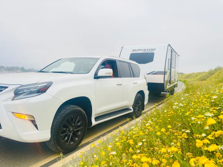 White SUV towing a Surveyor Legend RV rental on a scenic road lined with bright yellow wildflowers. Get ready for adventure!. Forest River Surveyor Legend 2023