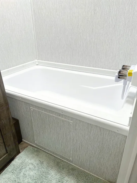 Experience comfort in your RV rental with this sparkling white bathtub, textured wall panels, and sleek faucet.. Forest River Wildwood X-Lite 2022