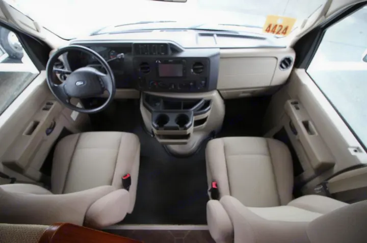 An RV rental's spacious front cab: Ford dashboard, steering wheel, cupholders, and tan driver/passenger seats.. Winnebago Access 2011
