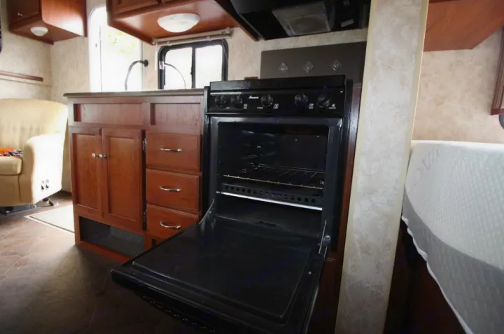 Inside an RV rental, showing the kitchen with an open oven, wood cabinets, and adjacent living/sleeping areas.. Winnebago Access 2011