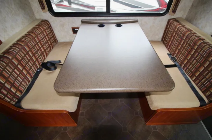 RV rental interior: cozy dinette area with a speckled table, built-in cup holders, and two patterned bench seats with seatbelts.. Winnebago Access 2011