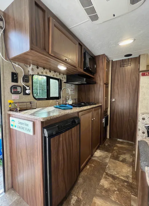 Modern RV rental kitchen with wood-look cabinets, stove, sink, and tiled floor, ready for your camping trip.. Coachmen Clipper 2016