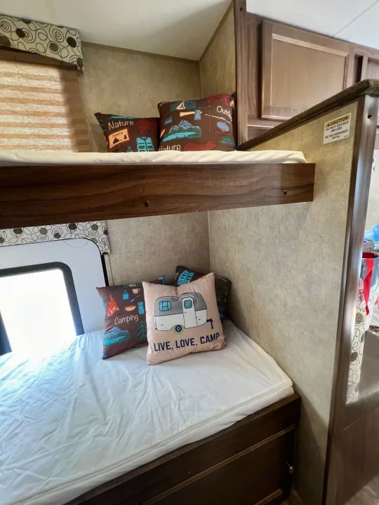 Cozy RV rental bunk beds with camping-themed pillows, perfect for family adventures. Max 300 lbs capacity.. Coachmen Clipper 2016