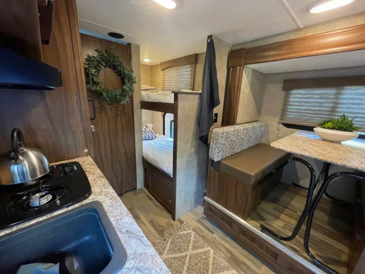 This cozy RV rental interior features a compact kitchen with a sink and stovetop, a dinette, and comfortable bunk beds.. Forest River Viking 2018