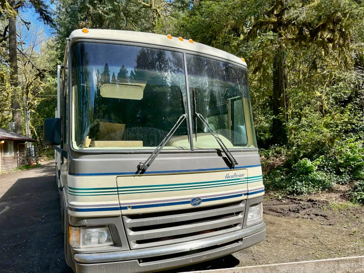 Front view of a classic Pace Arrow RV rental, white and gray with stripes, parked on a dirt drive amidst a dense, mossy forest.. Fleetwood Pace Arrow 1997